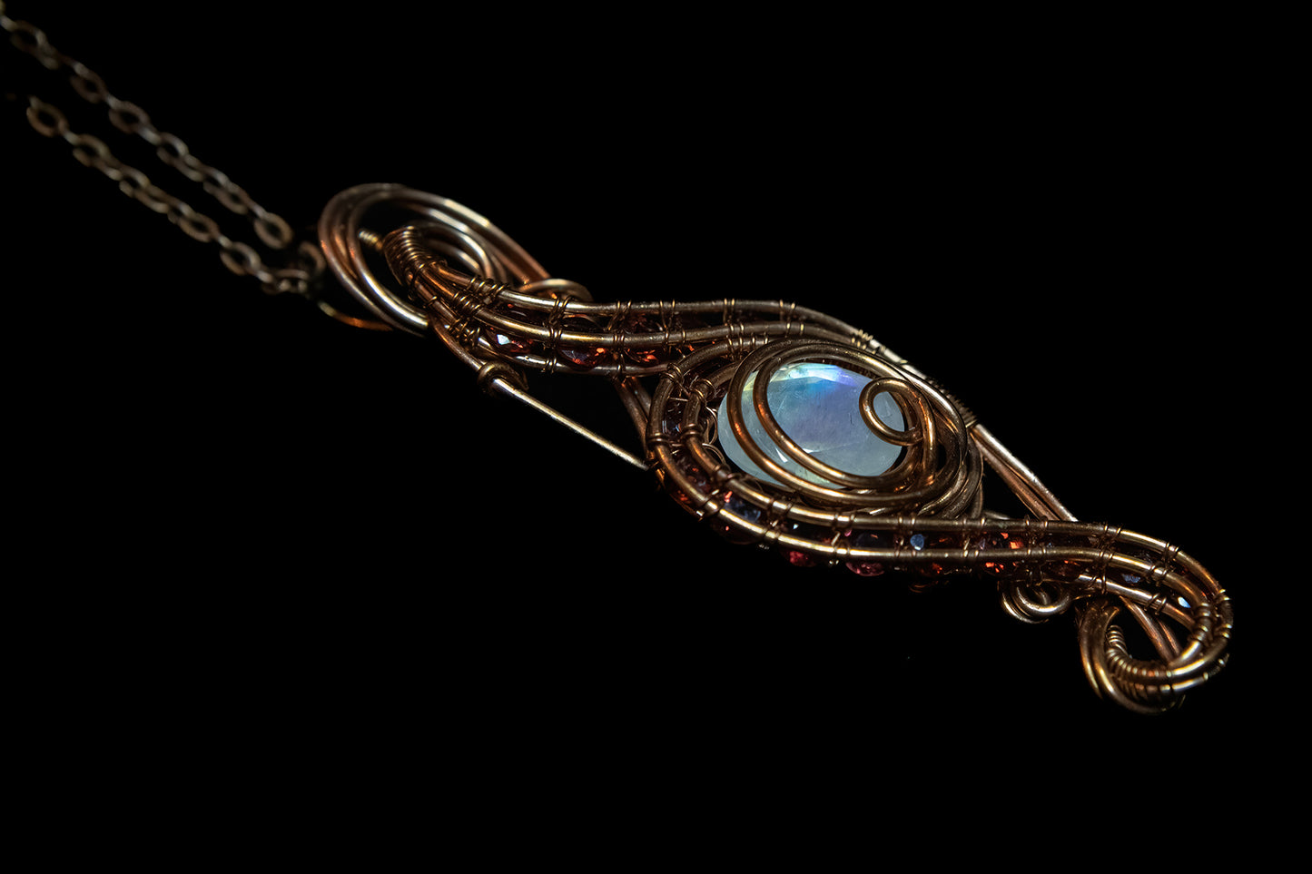 Faceted Madagascar Rainbow Flash Moonstone nestled in Fine Copper and surrounded by a multitude of Garnet Facets